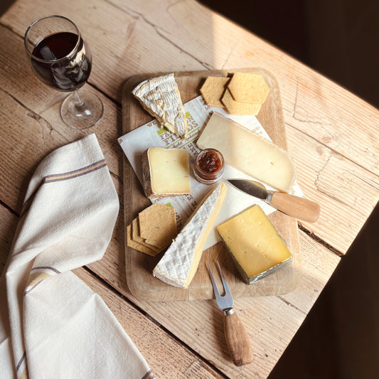 Assorted cheeses on a wooden board with a glass of red wine on a rustic wooden table.